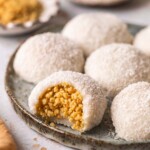 Coconut peanut mochi on plate with one mochi bitten open revealing granulated peanut filling.