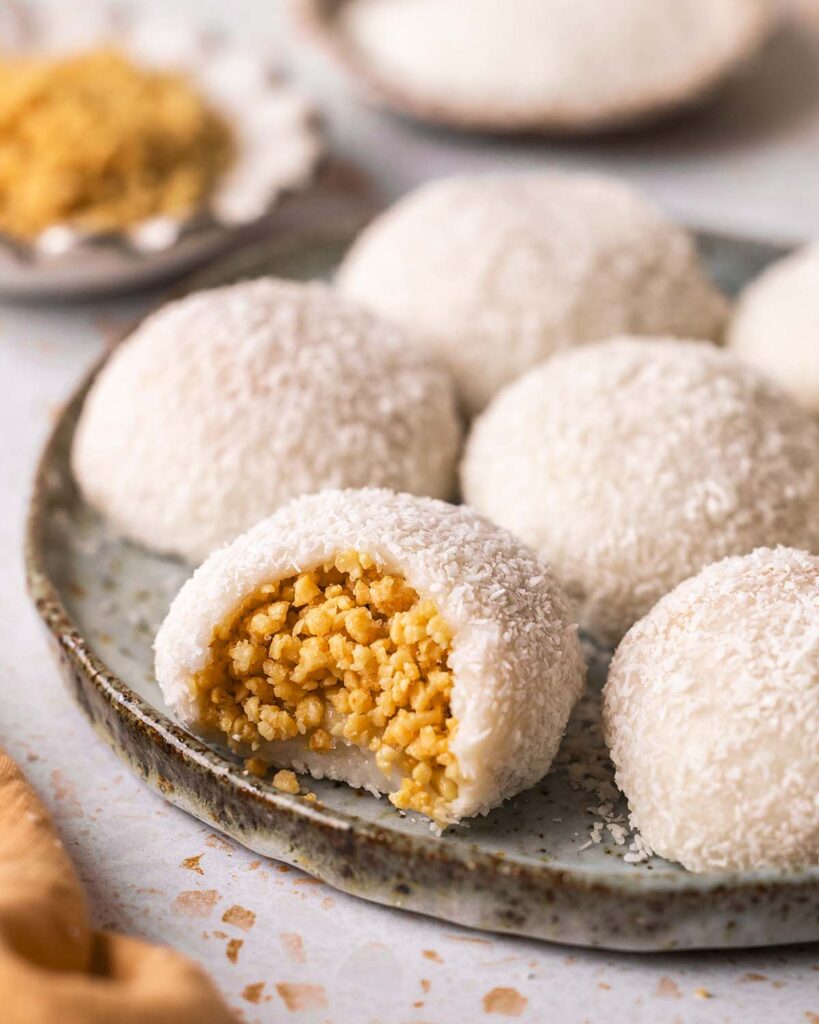 Coconut peanut mochi on plate with one mochi bitten open revealing granulated peanut filling.