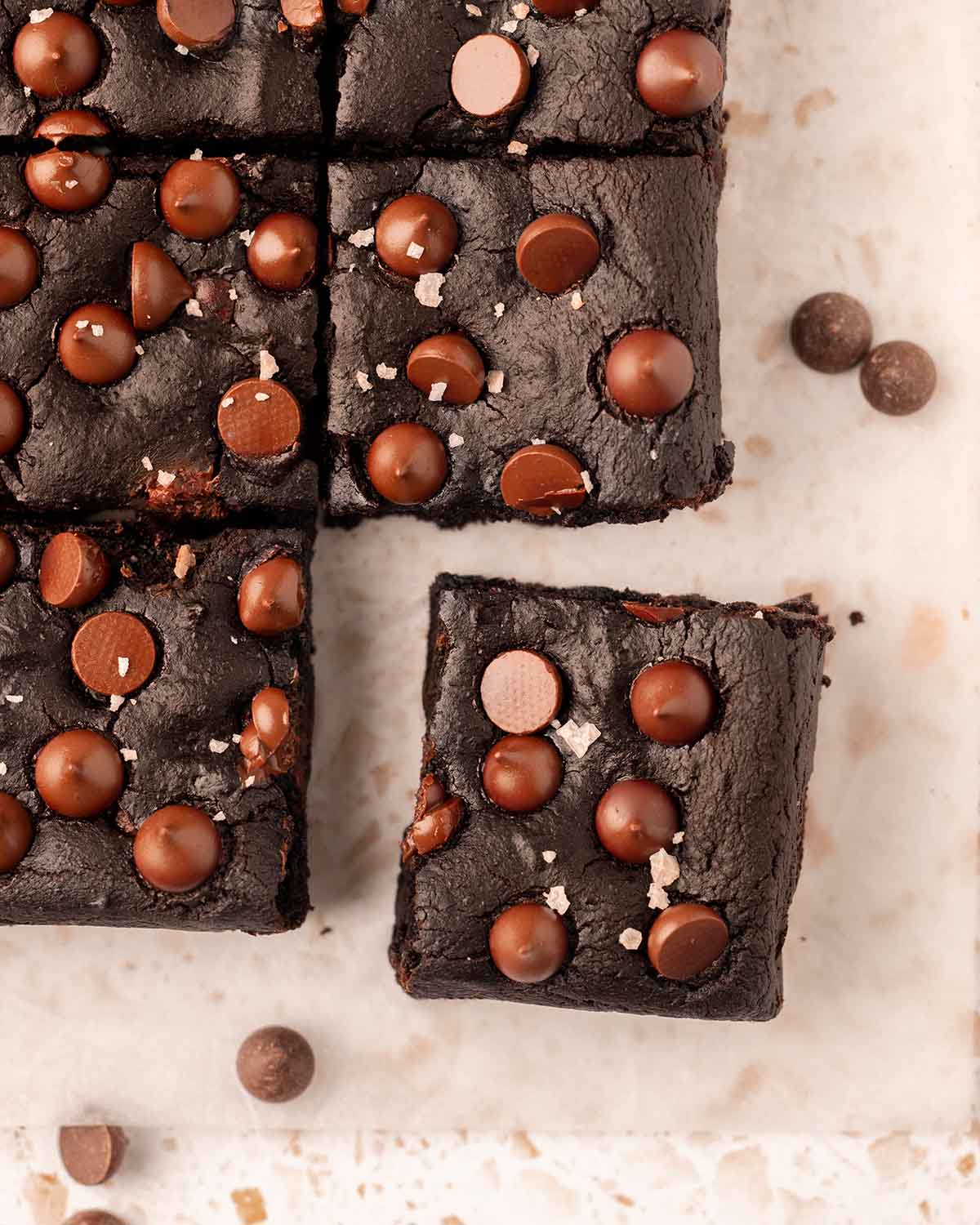 Black bean brownies with lots of chocolate chips. Brownies are on parchment paper with the corner brownie popping out.