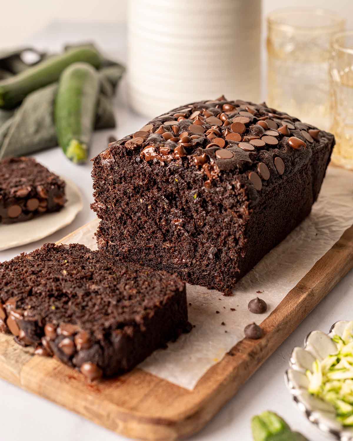 Chocolate zucchini bread on chopping board with one slice of the bread sliced off so you can see the rich and fluffy texture of the bread.