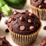 Close up of vegan chocolate zucchini muffin with a tall bakery-style top studded with mini chocolate chips.