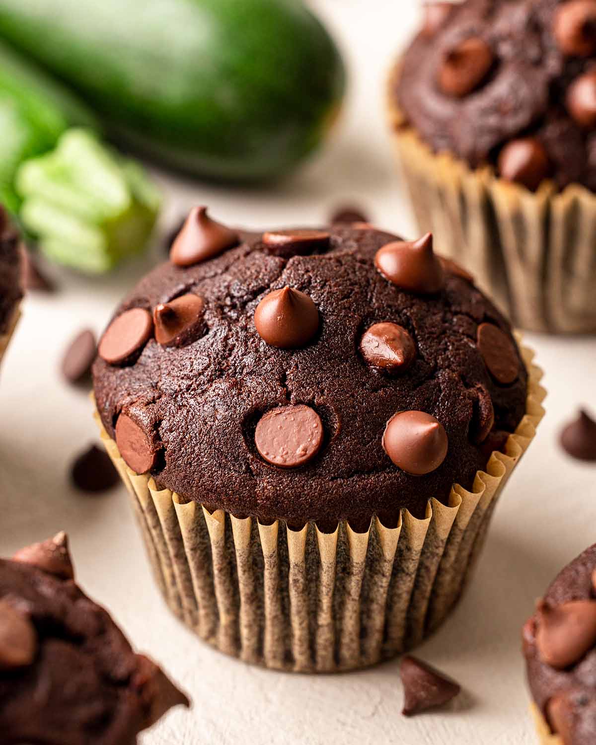 Close up of vegan chocolate zucchini muffin with a tall bakery-style top studded with mini chocolate chips.