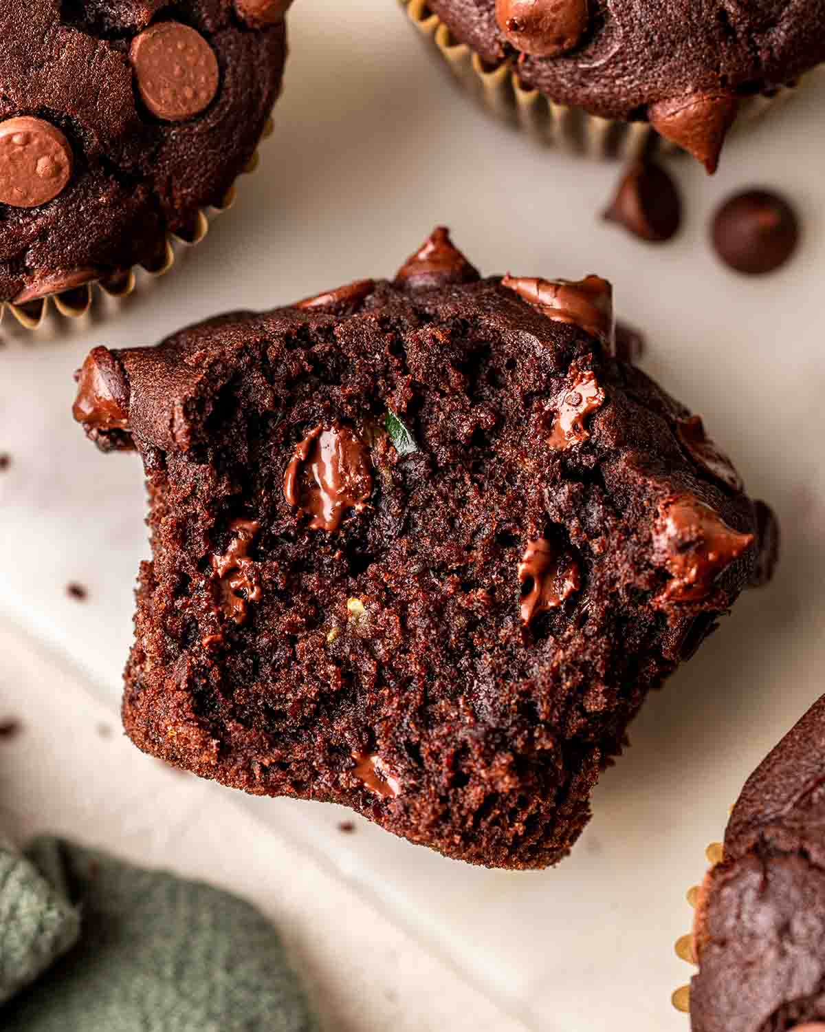 Close up of bitten muffin showing moist texture, gooey melted chocolate and little bits of shredded zucchini.