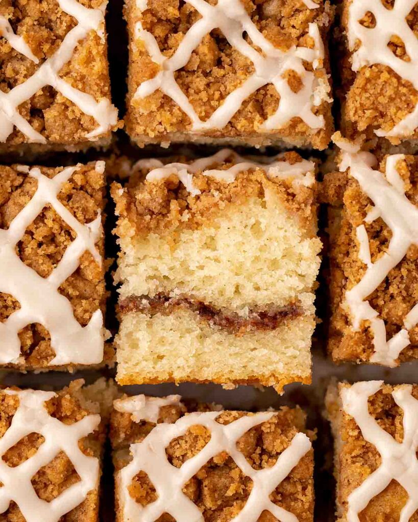 Overhead image of coffee cake cut into squares. The middle one is on the side showing its light fluffy texture and cinnamon sugar layer.