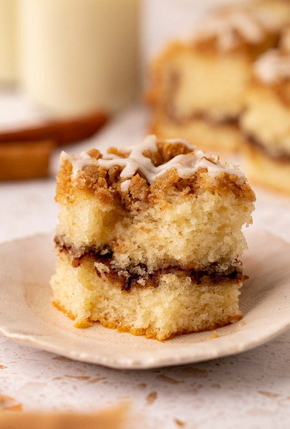 Close up of a slice of coffee cake that has a bite taken out of it. The cake has a light golden sponge, thick layer of cinnamon sugar and crumb topping.
