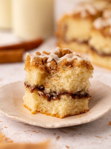 Close up of a slice of coffee cake that has a bite taken out of it. The cake has a light golden sponge, thick layer of cinnamon sugar and crumb topping.