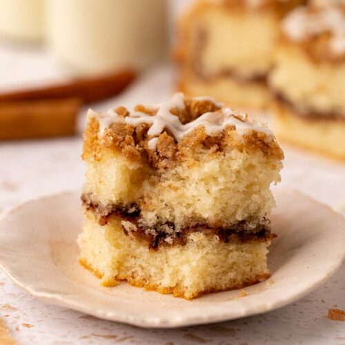 Close up of a slice of coffee cake that has a bite taken out of it. The cake has a light golden sponge, thick layer of cinnamon sugar and crumb topping.