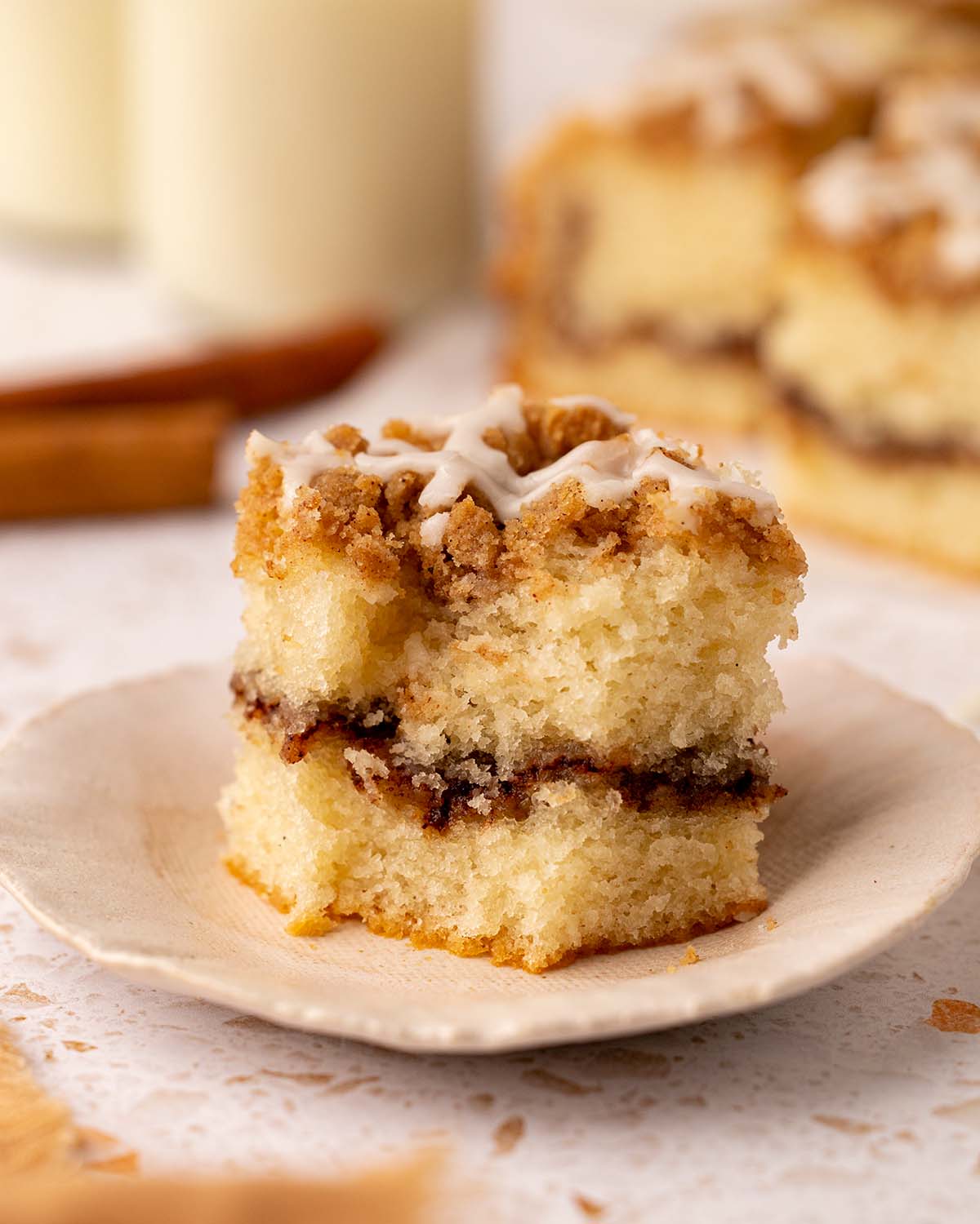 Close up of a slice of coffee cake that has a bite taken out of it. The cake has a light golden sponge, thick layer of cinnamon sugar and crumb topping.