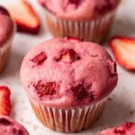 Close up of pink-colored strawberry muffin with chunks of strawberries baked into top of muffin.