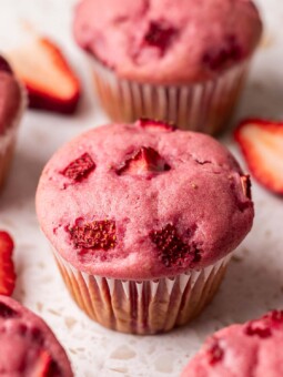 Close up of pink-colored strawberry muffin with chunks of strawberries baked into top of muffin.