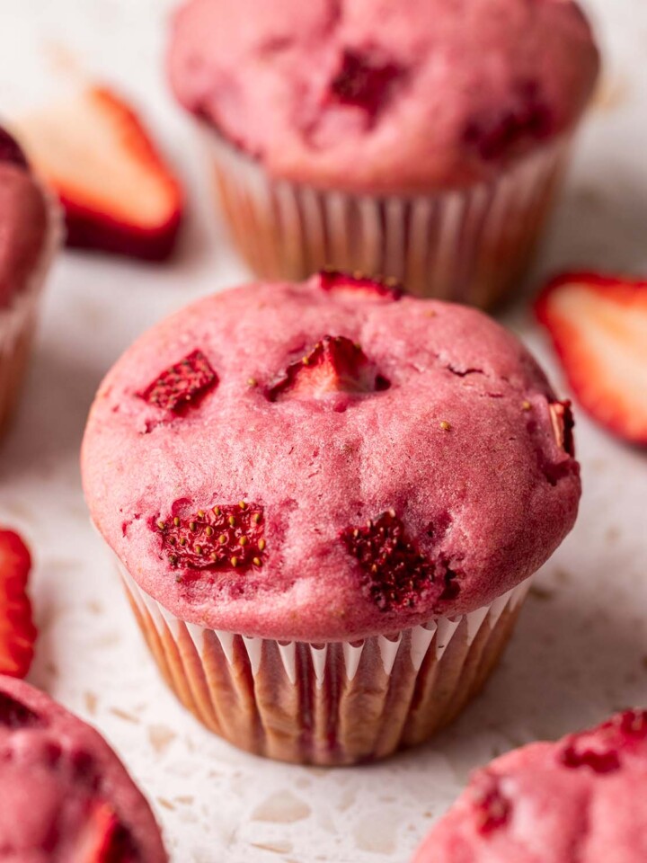Close up of pink-colored strawberry muffin with chunks of strawberries baked into top of muffin.