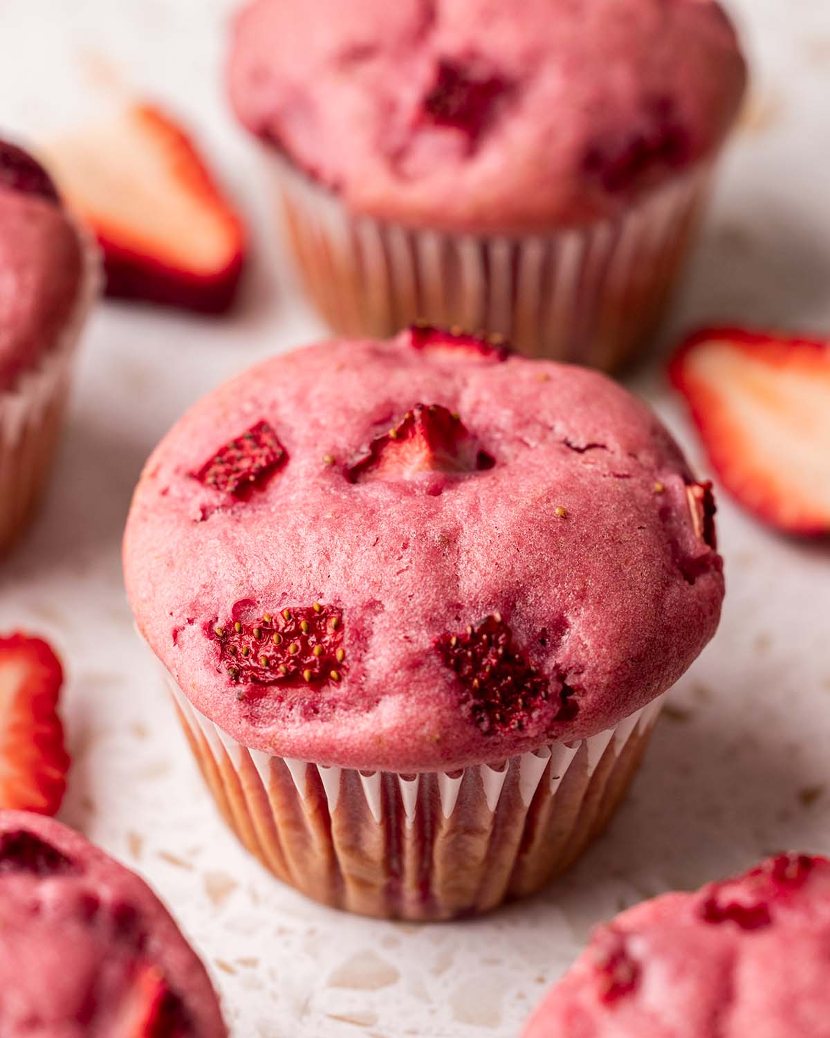 Close up of pink-colored strawberry muffin with chunks of strawberries baked into top of muffin.