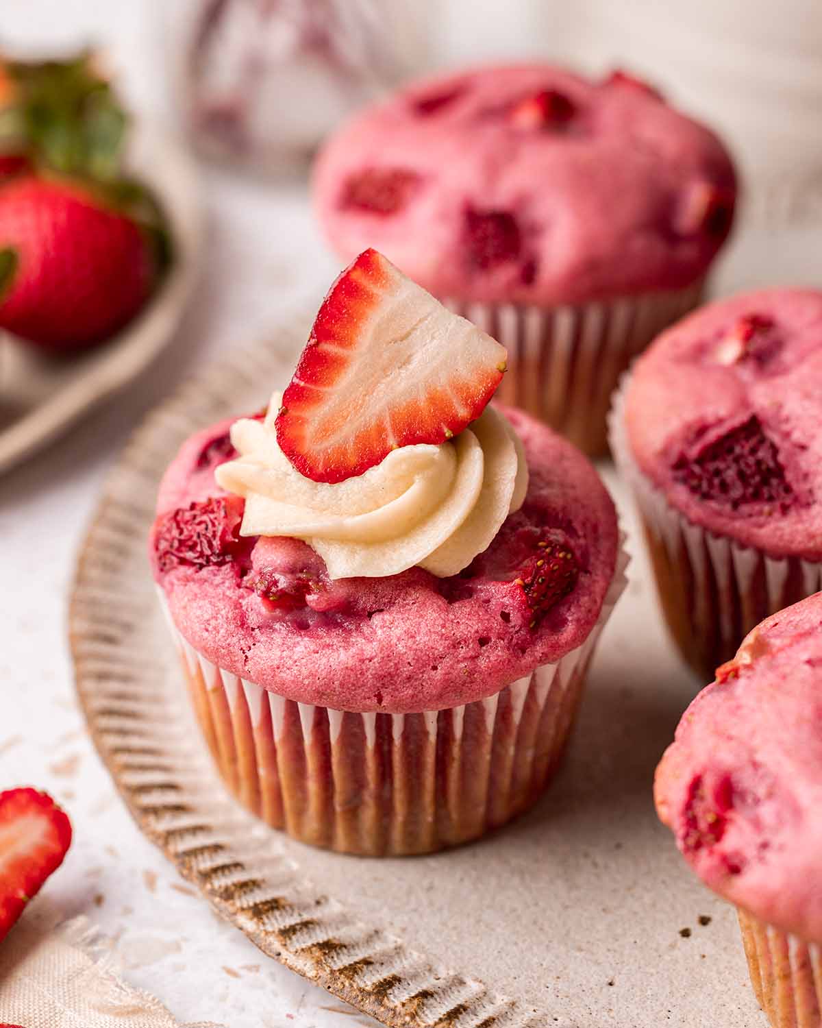 Close up of one pink muffin with a small amount of piped frosting and strawberry on top.