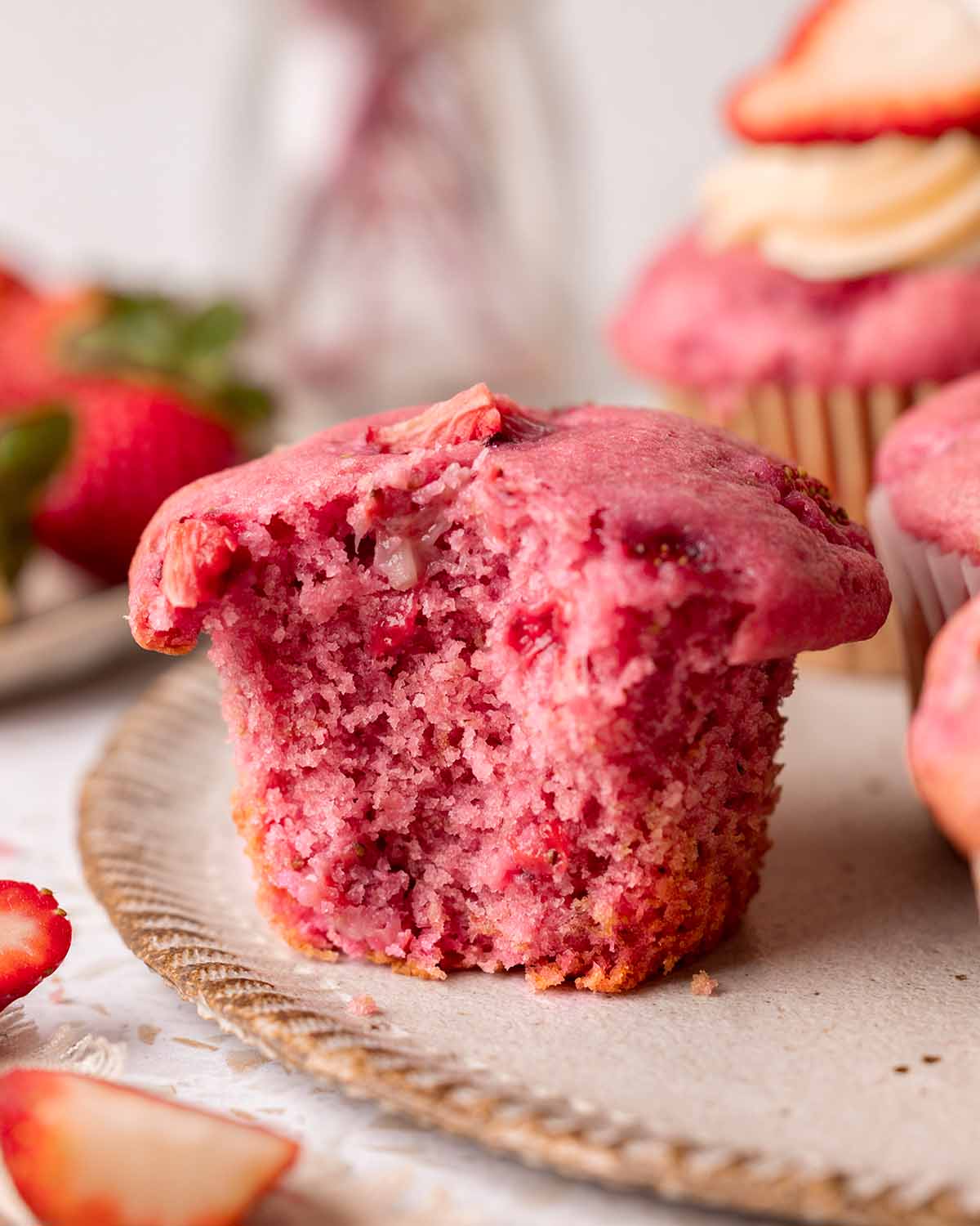 Close up of one double strawberry muffin with bite taken out showing fluffy texture and chunks of strawberries.