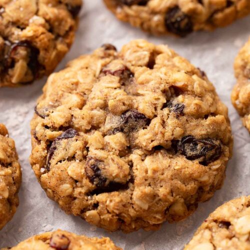 Close-up of oatmeal raisin cookies on crumpled parchment paper. The cookies are golden and thick.