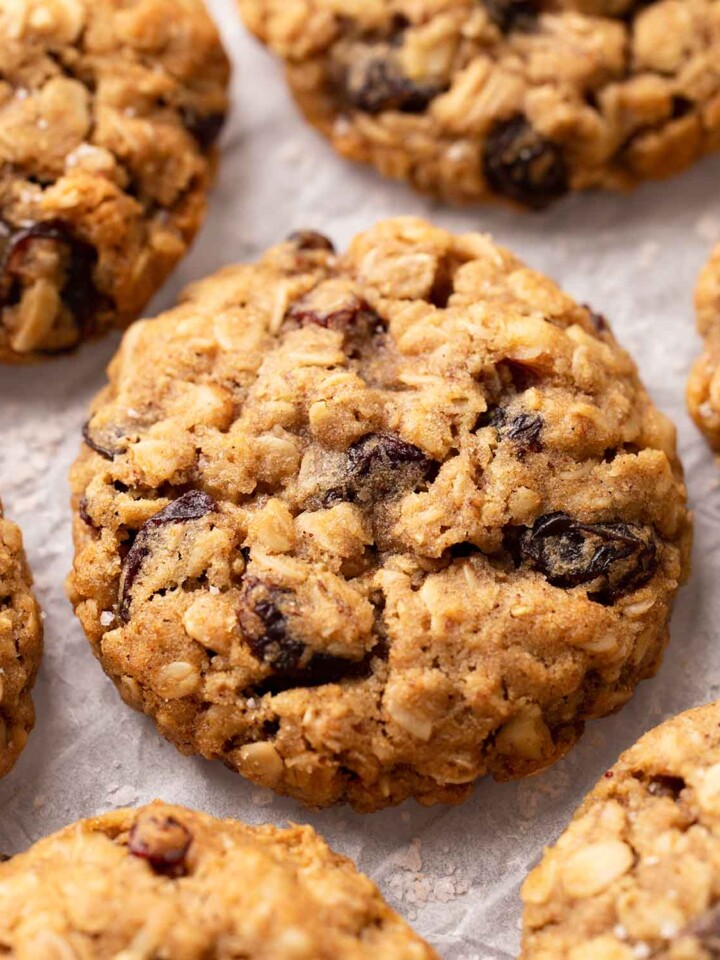 Close-up of oatmeal raisin cookies on crumpled parchment paper. The cookies are golden and thick.