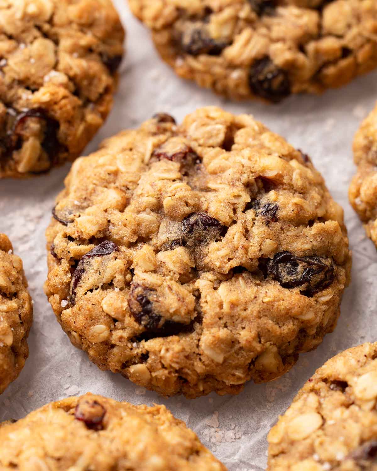 Close-up of oatmeal raisin cookies on crumpled parchment paper. The cookies are golden and thick.