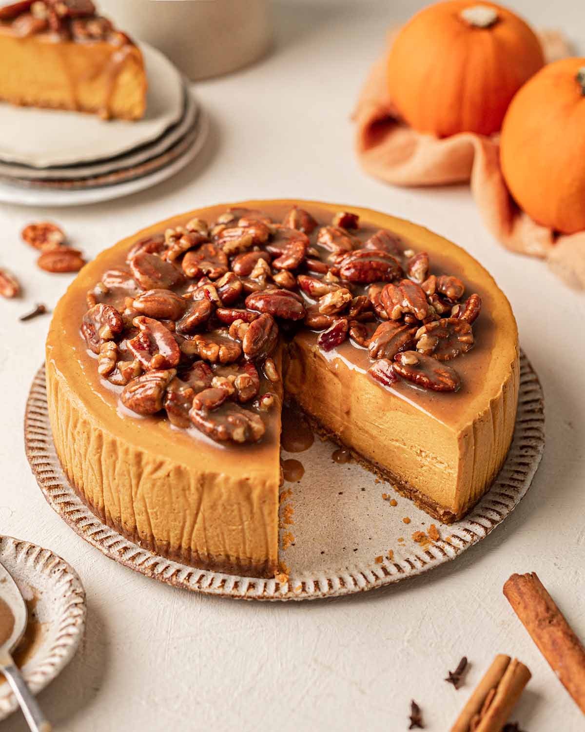 Vegan pumpkin cheesecake topped with a pecan caramel sauce. The cheesecake is on plate and there's a slice taken out to reveal the smooth creamy texture of the cheesecake.