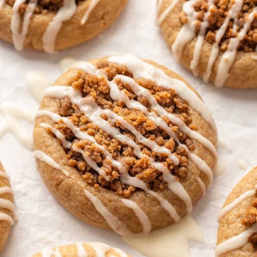 Close of of vegan coffee cake cookie with drizzle of runny white icing, on parchment paper.