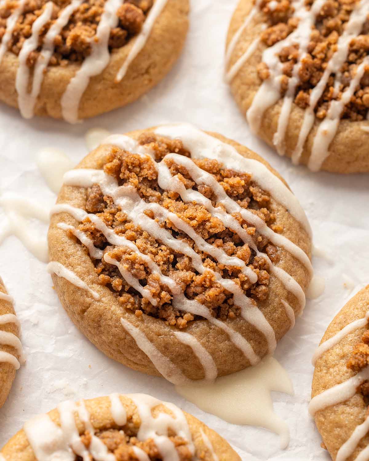 Close of of vegan coffee cake cookie with drizzle of runny white icing, on parchment paper.