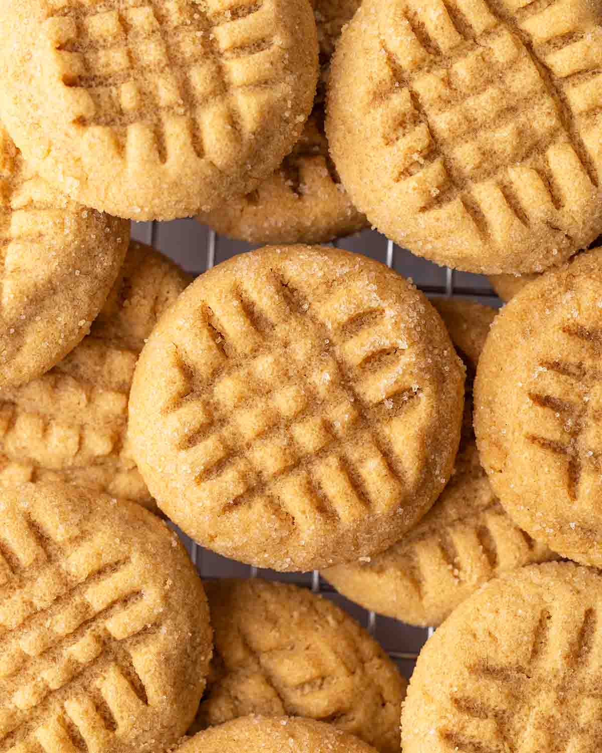 Overhead close up of peanut butter cookies on wire rack. Image focuses on criss cross pattern on cookies.