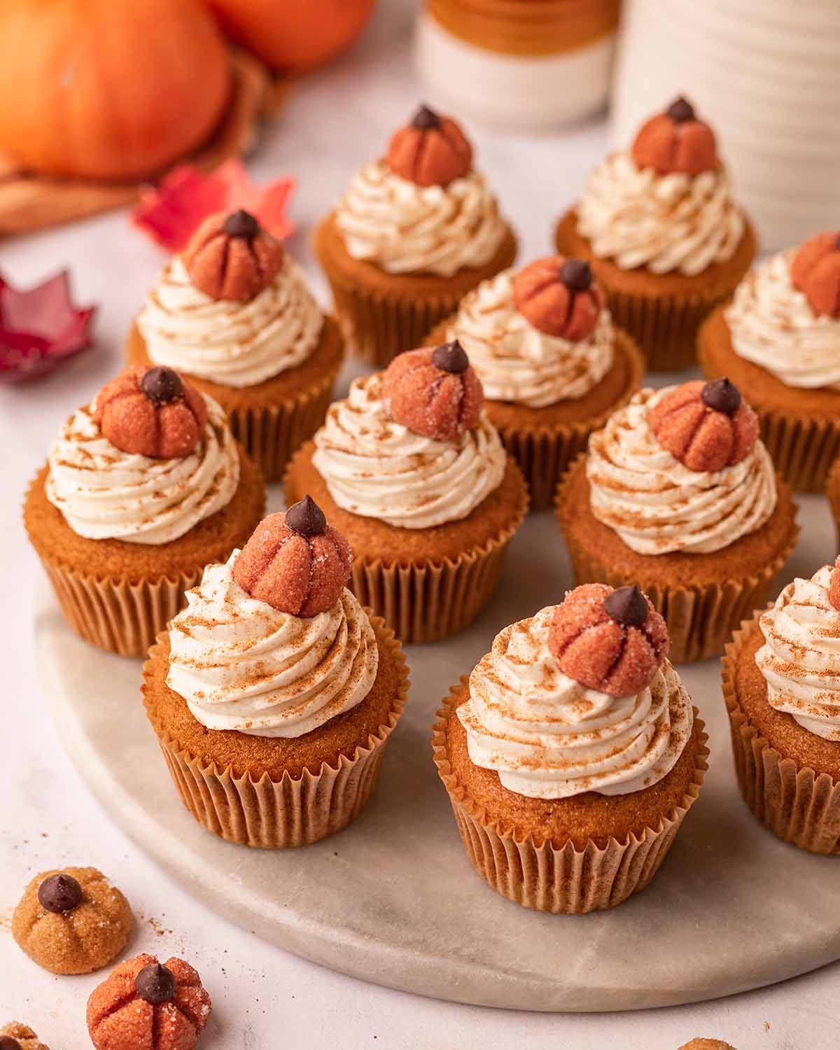 Many vegan pumpkin cupcakes with frosting and mini pumpkins on top, on marble serving board.