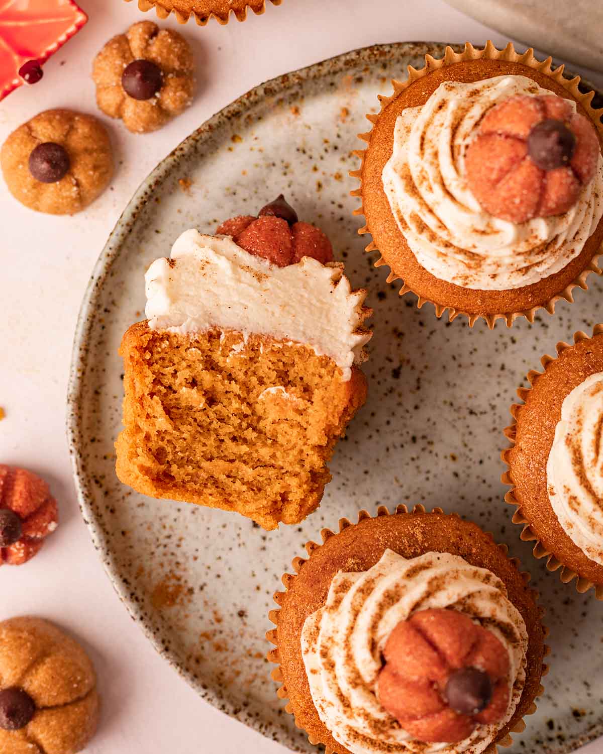 Half of a pumpkin cupcake on its side showing its fluffy texture. Cupcake is on plate with other cupcakes.