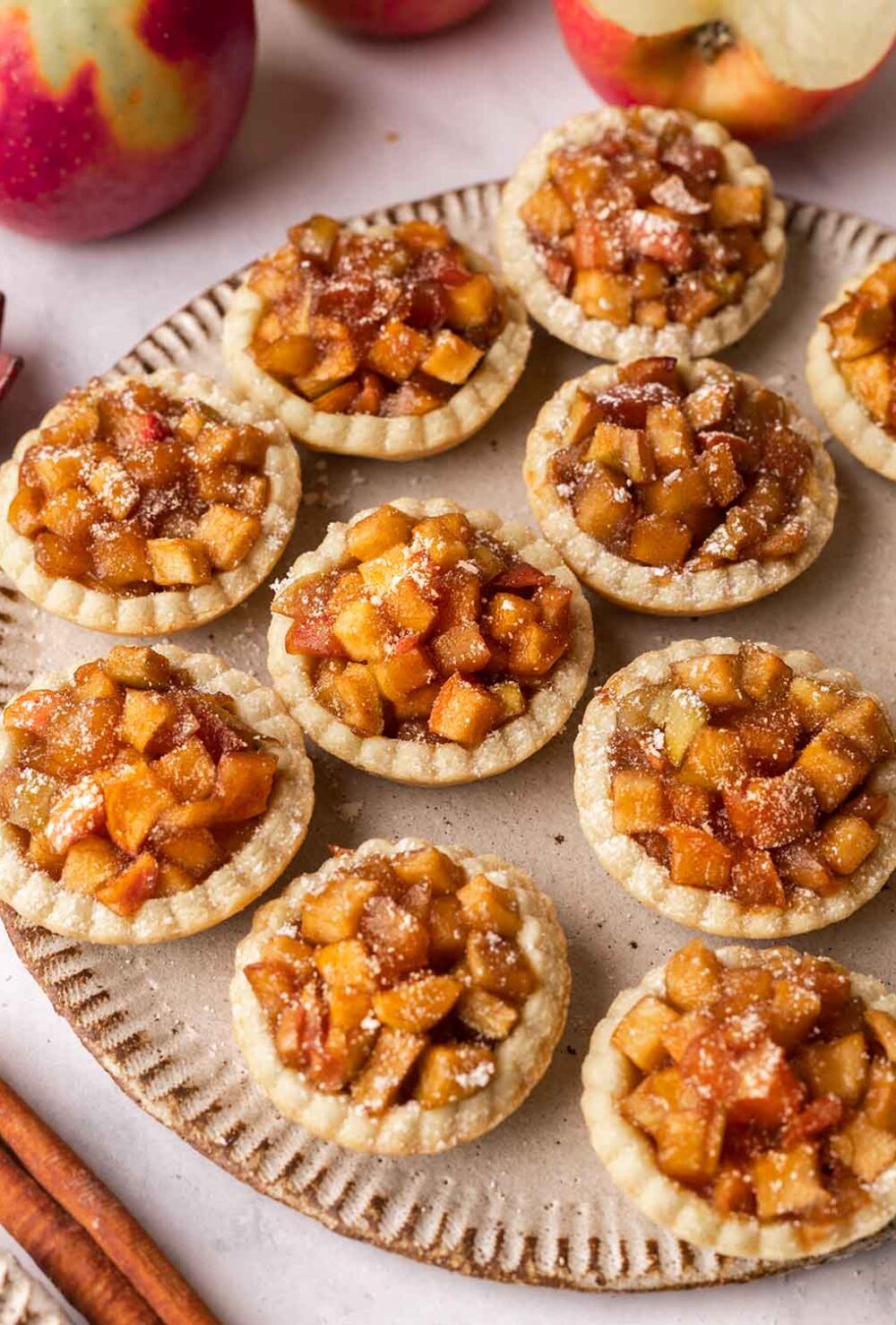 Several mini apple tarts dusted with powdered sugar on a rustic gray plate.