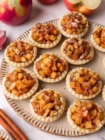Several mini apple tarts dusted with powdered sugar on a rustic gray plate.