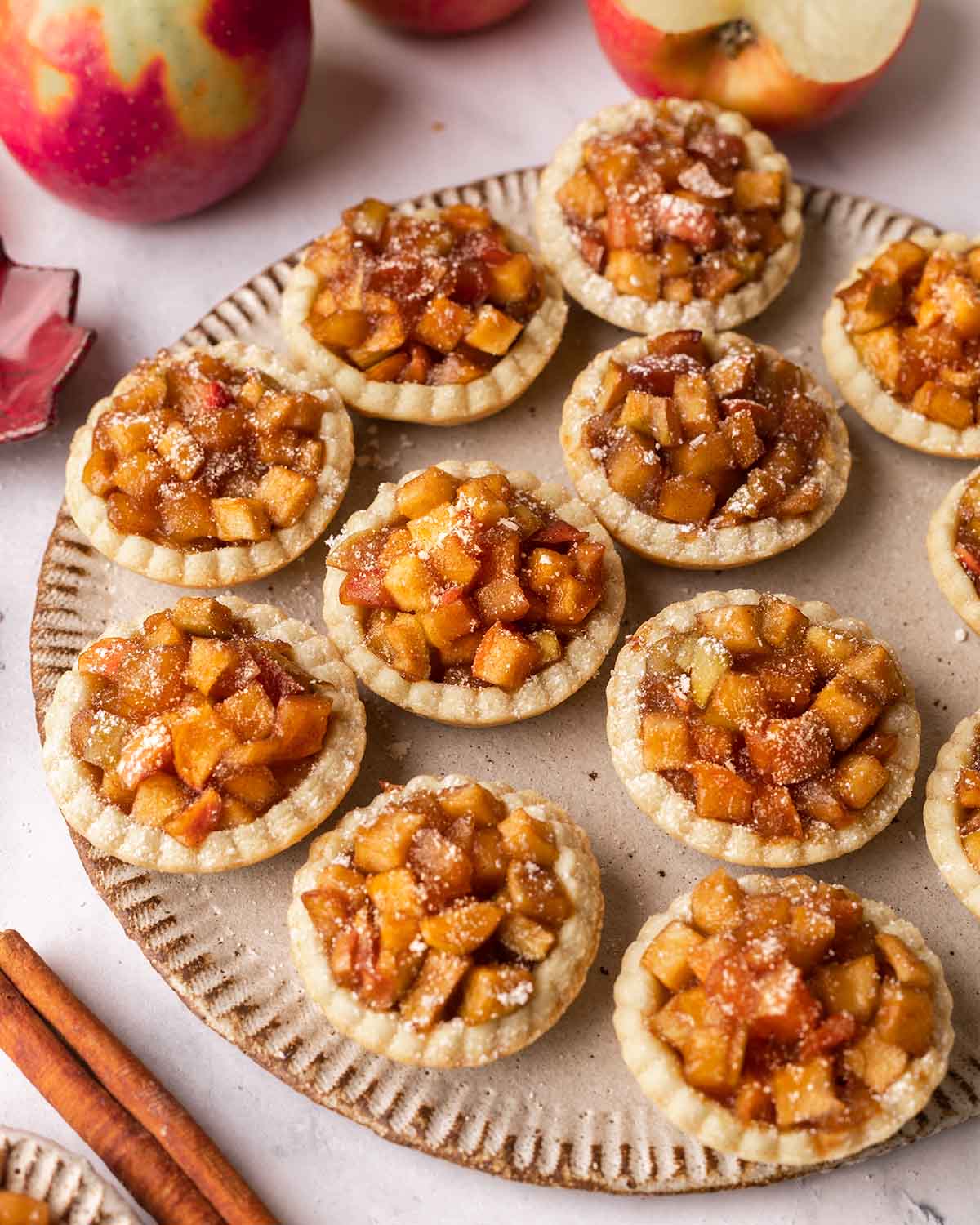 Several mini apple tarts dusted with powdered sugar on a rustic gray plate.