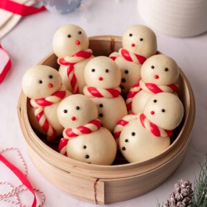 Seven steamed snowmen buns upright in a bamboo steamer.