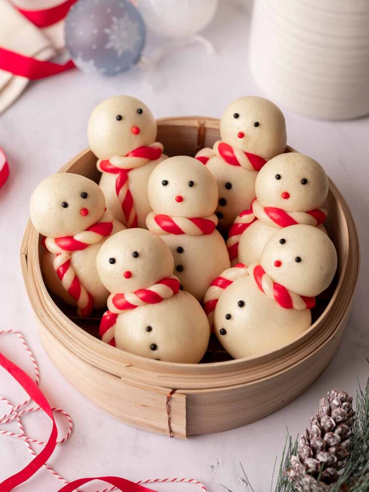 Seven steamed snowmen buns upright in a bamboo steamer.
