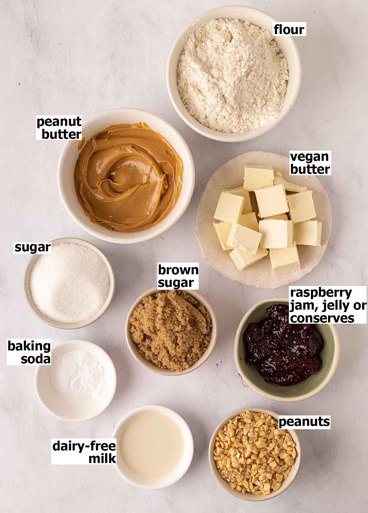Flat-lay of ingredients in small dishes for veagn peanut butter jelly cookies.