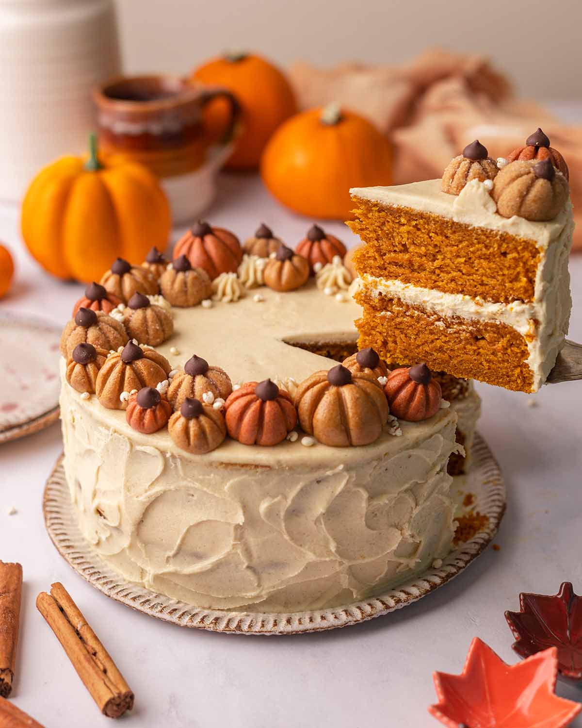 Cake decorated with mini orange and brown pumpkins and with one cake slice cut out being lifted up.