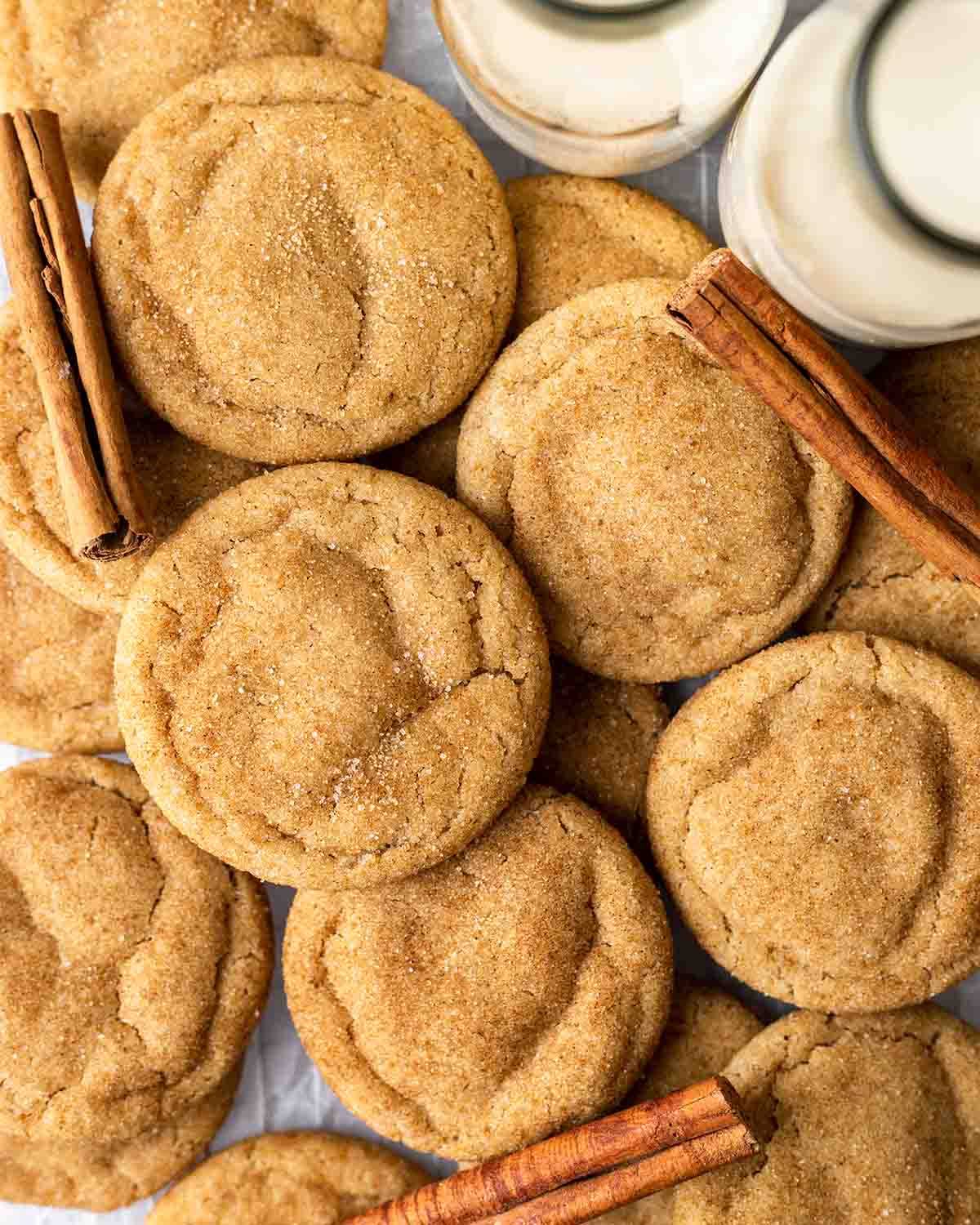 Flatlay of many snickerdoodles layered on top of each other, with cinnamon sticks on the side.