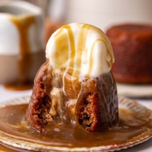 Individual sticky date with scoop of ice cream and generous amount of toffee sauce on pudding and plate.