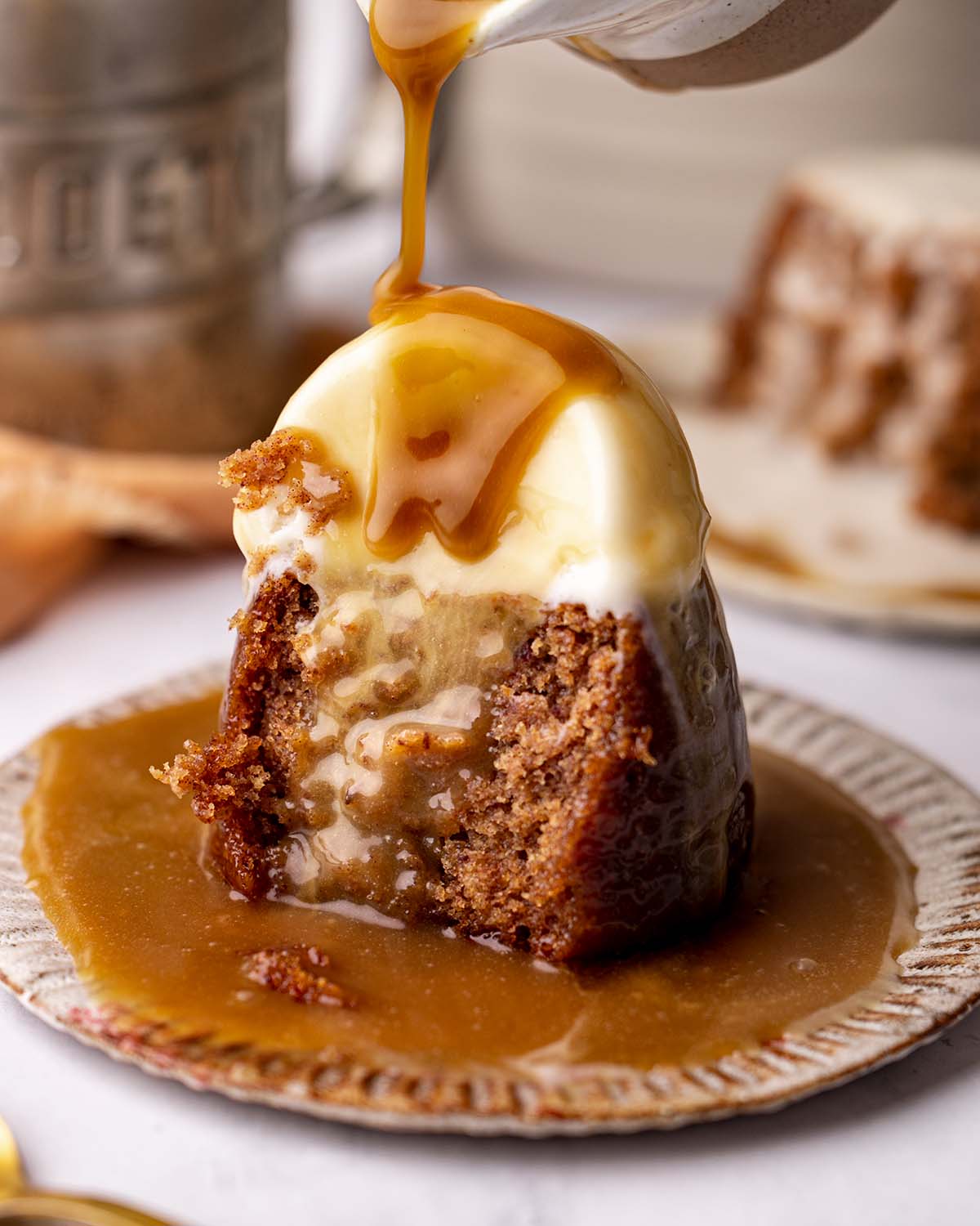 Sticky date pudding with scoop of ice cream with toffee sauce poured on top.