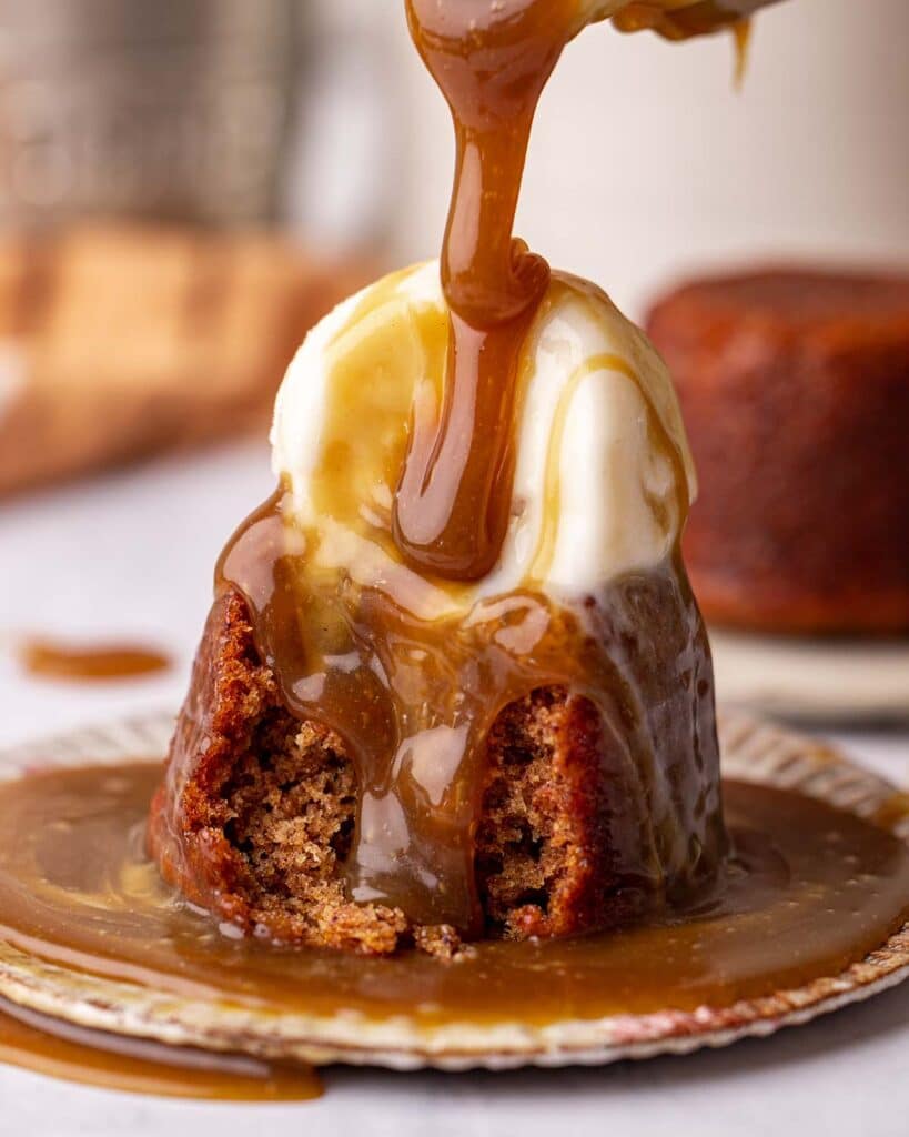 Close up of individual sticky date pudding with scoop of ice cream with toffee sauce poured on top.