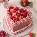 Heart-shaped with cool baby pink frosting and piped white frosting, and lots of fresh rapsberries and strawberries on top.