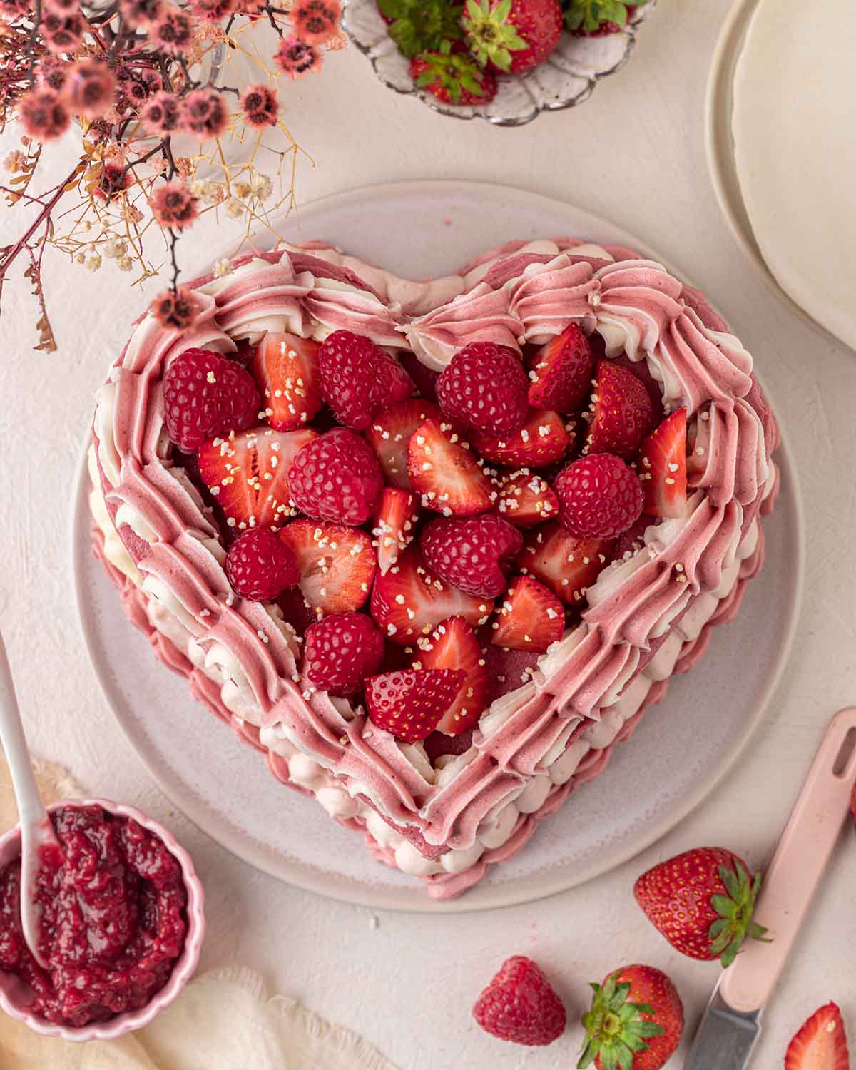 Overhead image of heart cake focusing on the piped pink and white frosting around border of cake and topping of fresh raspberries and strawberries.