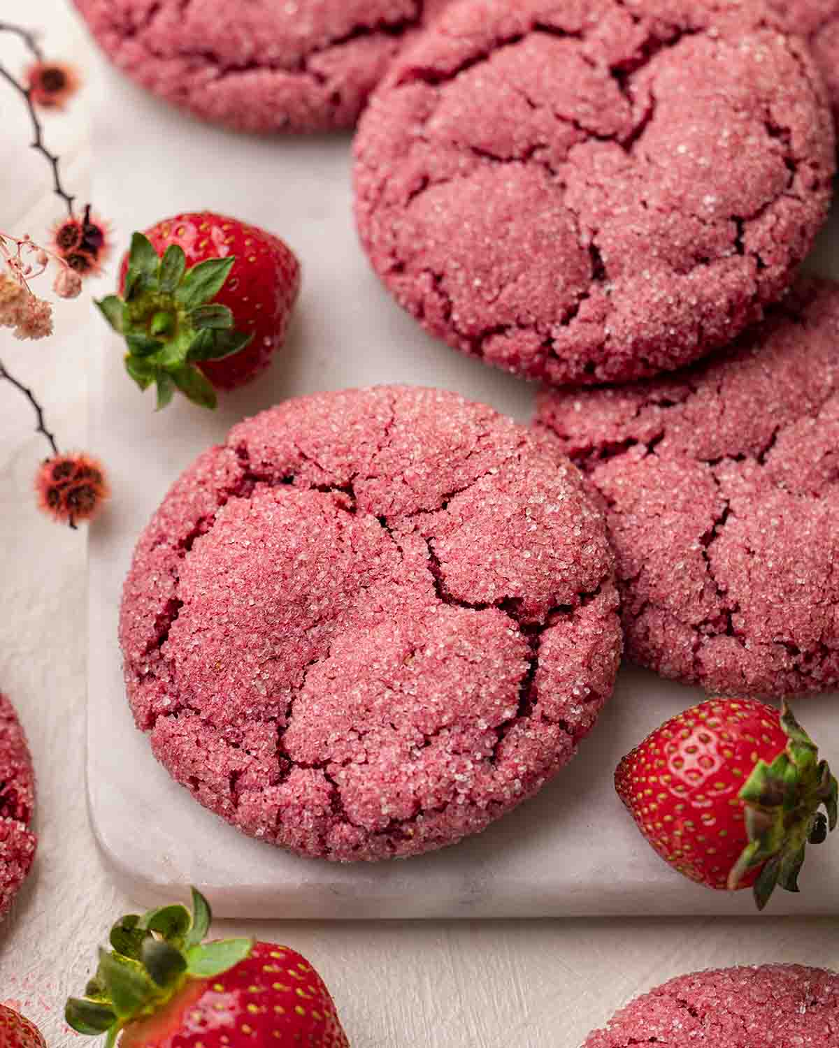 Close up of pink strawberry cookies with crackly sugar sugar on marble serving board.