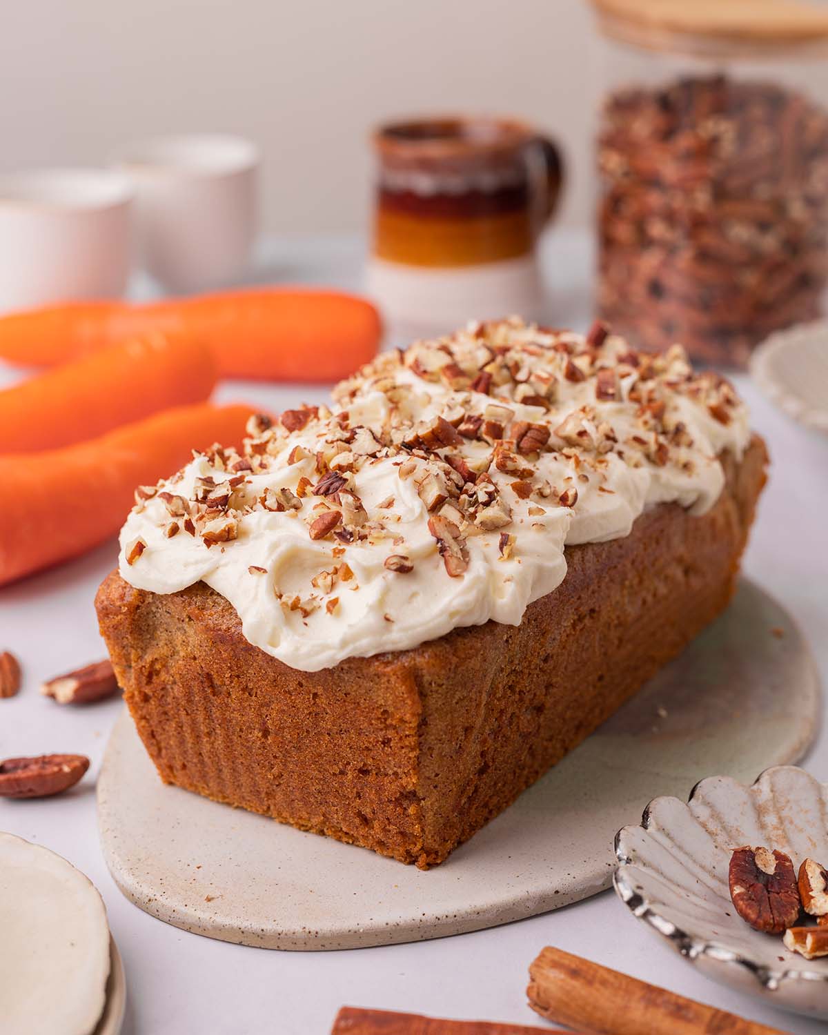 Whole carrot cake loaf on serving board. The loaf is rustically topped with creamy white icing and chopped pecans.