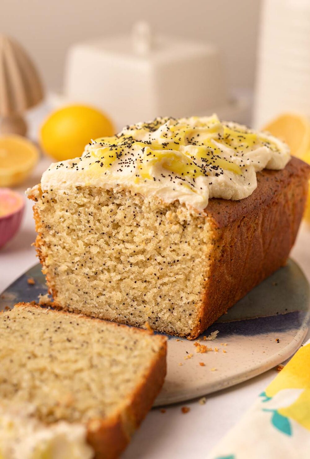 Lemon poppy seed loaf cake on oval serving board. The cake has a slice cut off revealing the fluffy golden texture of the cake.