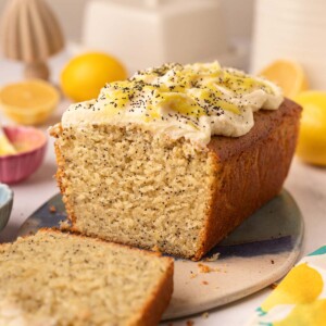 Lemon poppy seed loaf cake on oval serving board. The cake has a slice cut off revealing the fluffy golden texture of the cake.