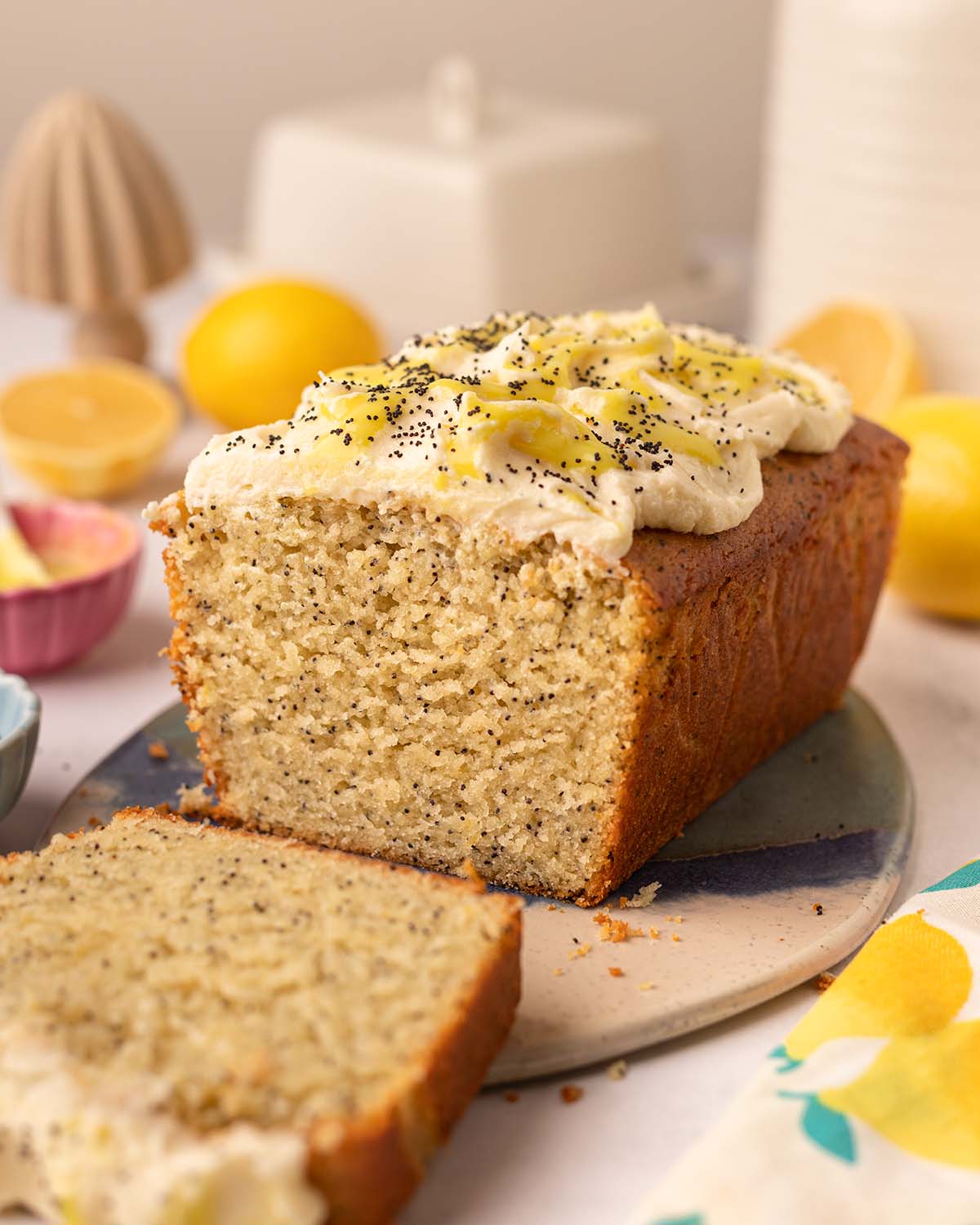 Lemon poppy seed loaf cake on oval serving board. The cake has a slice cut off revealing the fluffy golden texture of the cake.