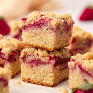 Stack of two cake squares, each with layers of a golden cake, jammy strawberries and crumb topping.