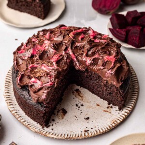 Chocolate beetroot cake on plate with two slices cut out. Cake is topped with rustic chocolate and beetroot frosting.