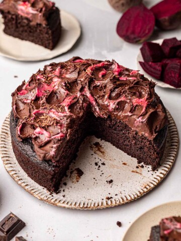 Chocolate beetroot cake on plate with two slices cut out. Cake is topped with rustic chocolate and beetroot frosting.