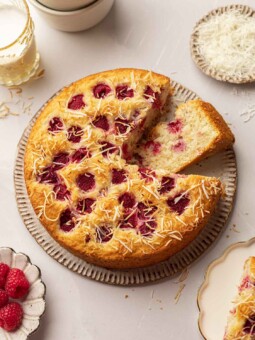 Raspberry coconut cake on rustic plate. One slice has been cut out and placed on its side showing the golden fluffy texture of the cake.