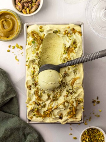 Overhead image of loaf pan filled with the pistachio ice cream with a scoop of ice cream removed to show the soft texture.